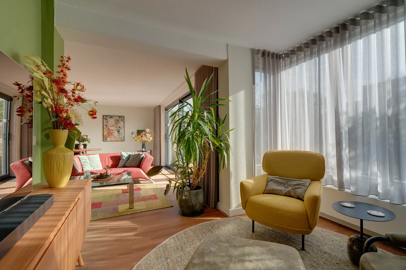 Lichte woonkamer met gele fauteuil, planten en vitrage voor een grote raampartij